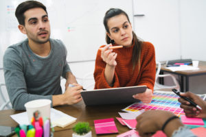 Deux professionnels en réunion, un homme et une femme, discutant des échantillons de couleurs avec des notes adhésives et des documents sur la table.