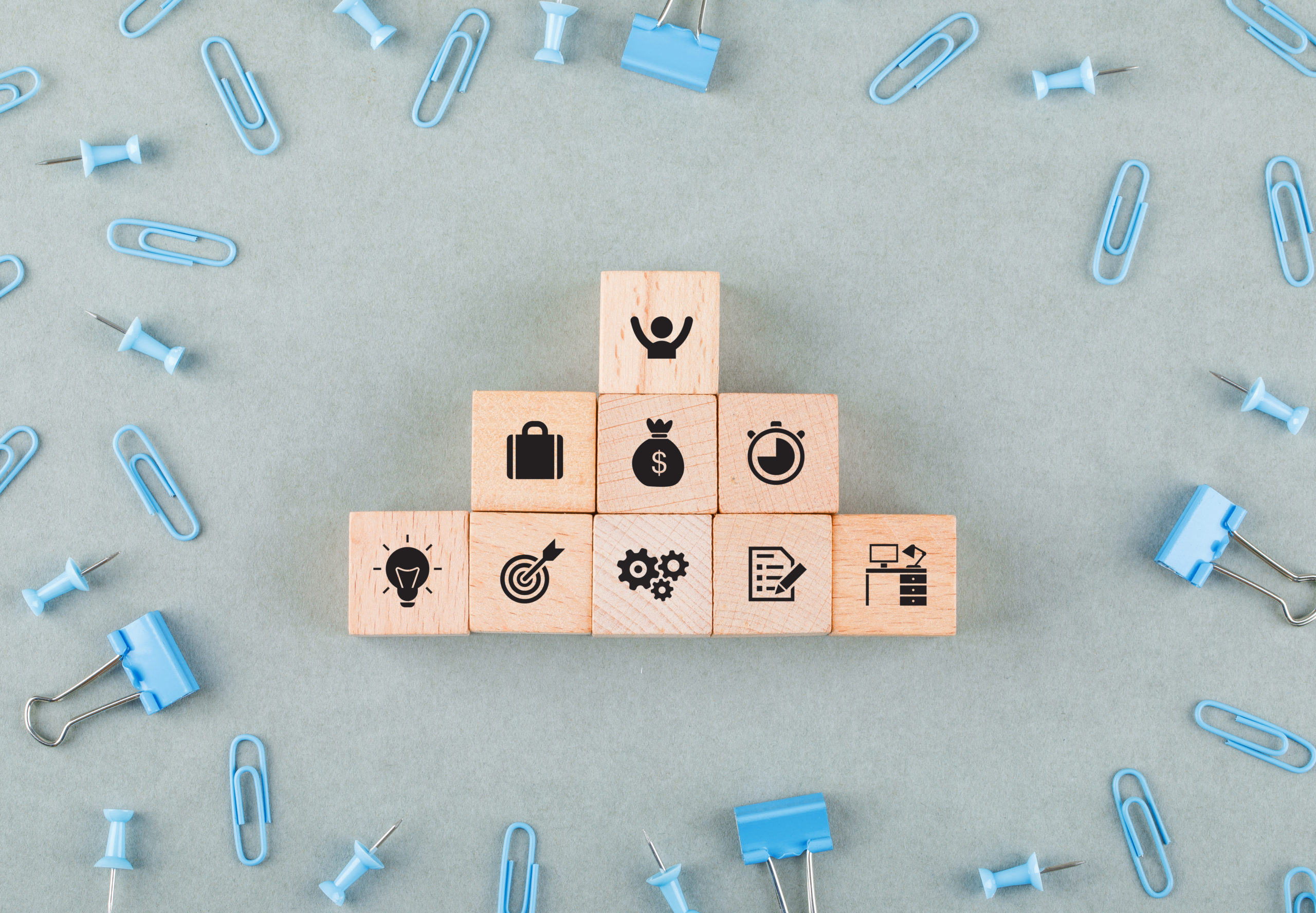 Des cubes en bois avec des icônes d'entreprise sur un bureau entourés de trombones et de punaises, représentant les concepts d'affaires et de stratégie."