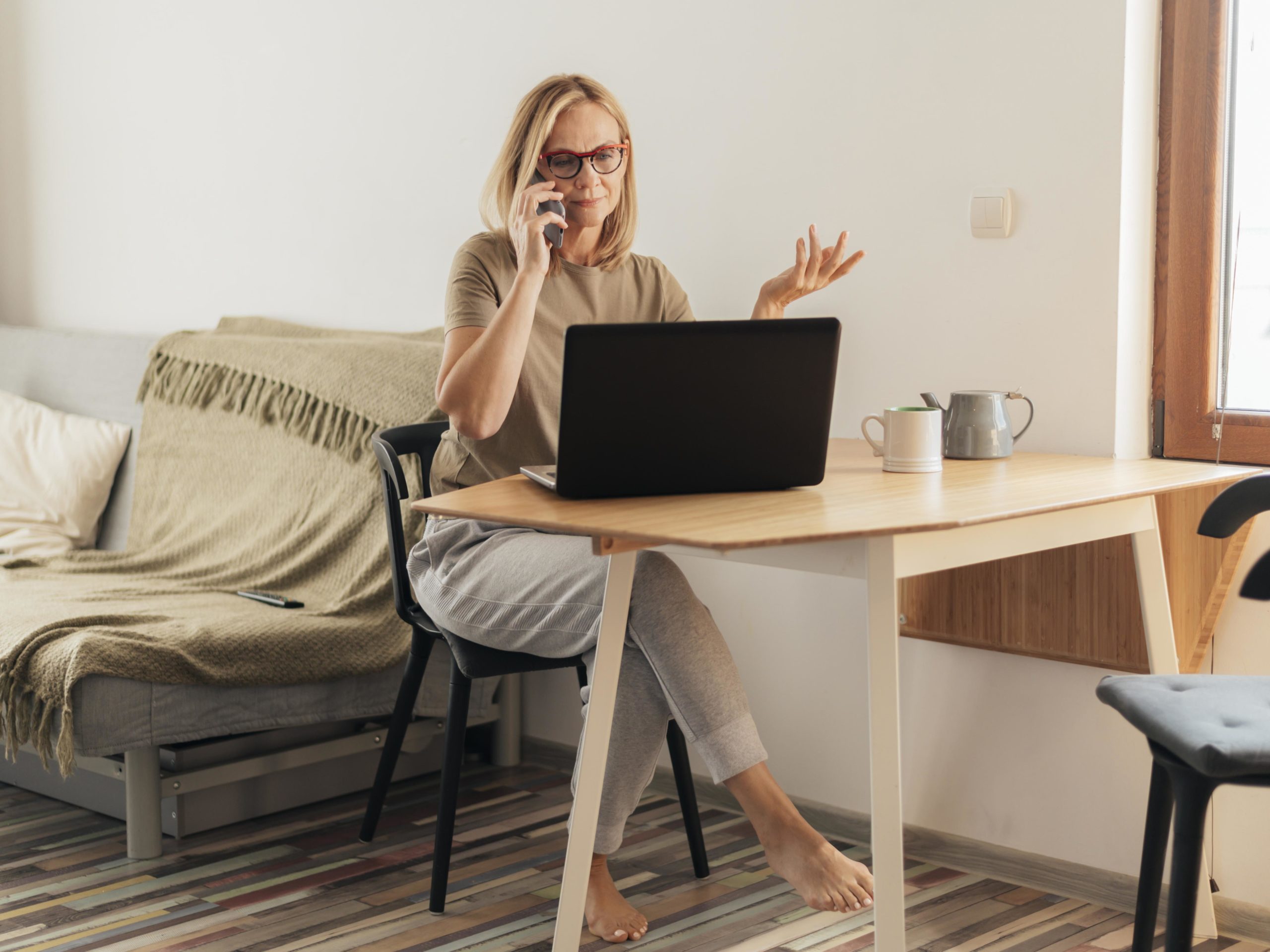 Femme en télétravail devant un ordinateur portable, parlant au téléphone dans un espace de travail à domicile